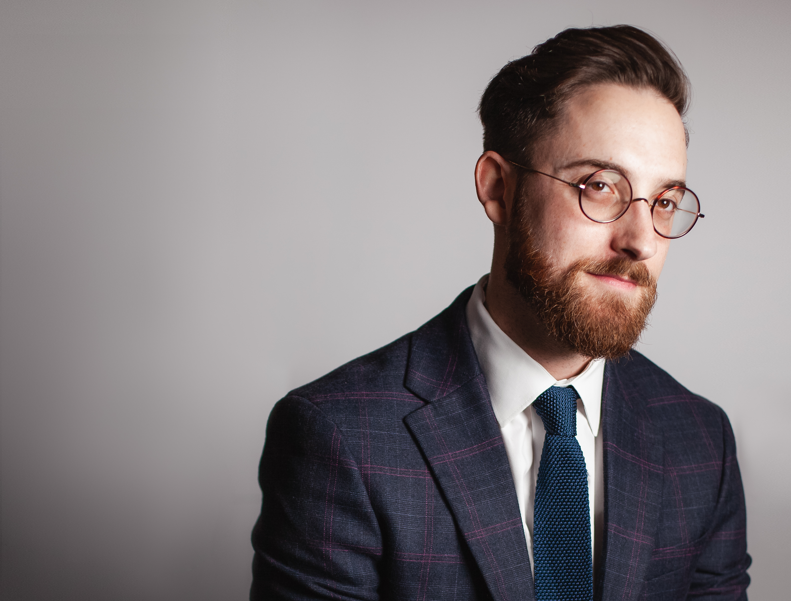 Drew Feldman wearing glasses, a dark checked suit, and a blue tie.